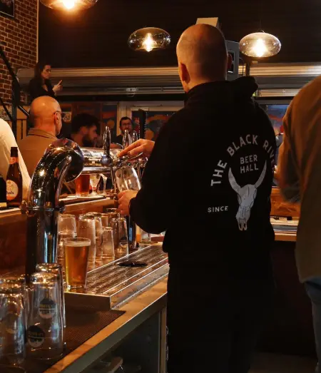 Barman en sweat The Black River servant des bières au comptoir