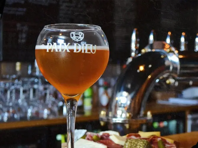 Verre de bière ambrée devant les tireuses, avec une planche de charcuterie